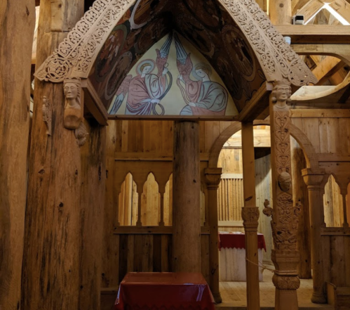 Interior of a wooden structure featuring intricate carvings and colorful murals on the ceiling.