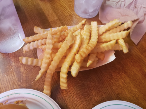A serving of golden, crinkle-cut fries on a paper tray, with glasses of water in the background.