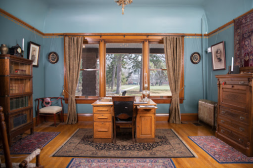A vintage office with a wooden desk, bookshelves, and large windows, featuring blue walls and decorative rugs.