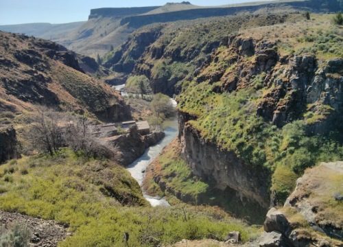 A scenic view of a winding river surrounded by steep, rocky cliffs and lush greenery under a clear blue sky.