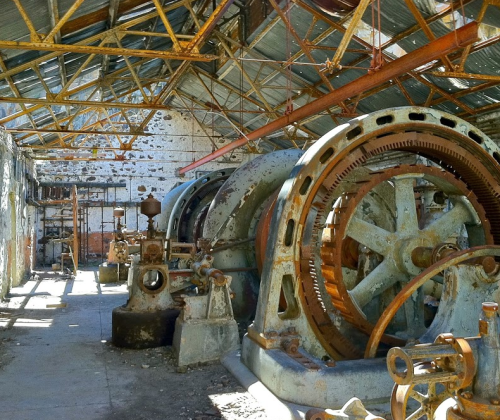 Abandoned industrial space with large, rusted machinery and a weathered roof, showcasing decay and neglect.