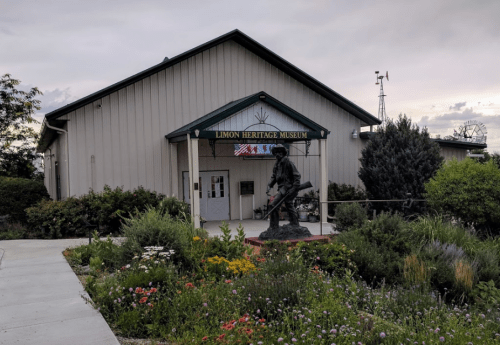 Exterior of the Limon Heritage Museum, featuring a statue and surrounded by colorful flowers and greenery.