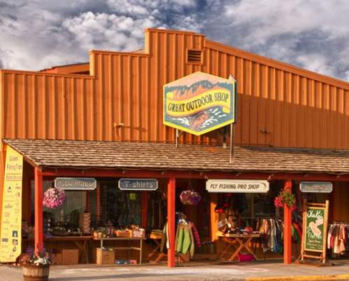 A colorful outdoor shop with a sign, displaying fishing gear and apparel, under a cloudy sky.