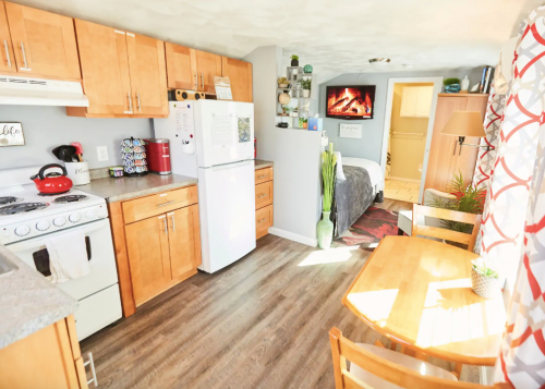 Cozy kitchen and dining area with wooden cabinets, a table, and a view of a bedroom in a well-lit space.