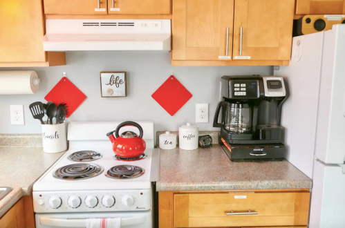 Cozy kitchen with wooden cabinets, a red kettle, coffee maker, and decorative wall art.