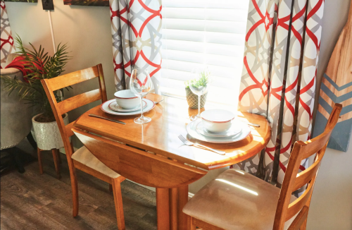 A cozy dining setup with a wooden table, two chairs, and elegant tableware by a window with patterned curtains.