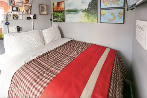Cozy bedroom with a checkered bedspread, white pillows, and colorful wall art, including maps and landscapes.