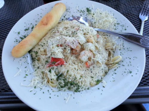 A plate of creamy shrimp pasta topped with cheese and herbs, accompanied by a breadstick on the side.