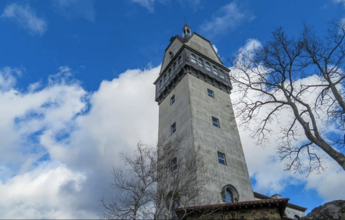 A tall, historic tower against a blue sky with clouds, surrounded by bare trees.