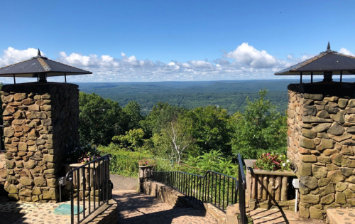 Scenic view from stone gates overlooking lush green hills and a blue sky with scattered clouds.
