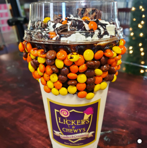 A large cup of dessert topped with whipped cream, chocolate drizzle, and colorful candy-coated chocolates.