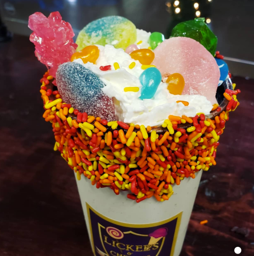 A colorful dessert cup topped with whipped cream, candy, and vibrant sprinkles.