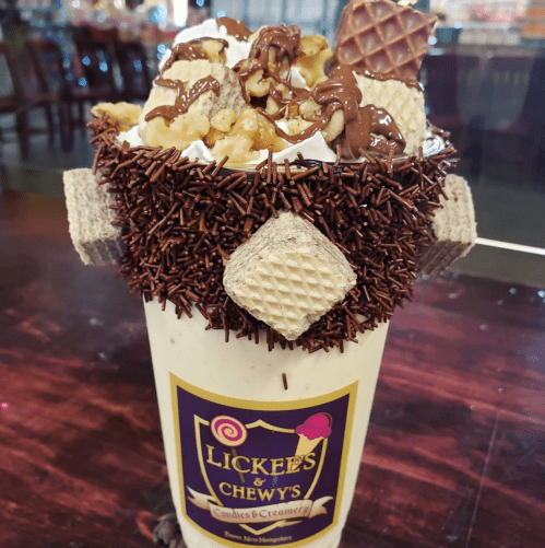 A decadent milkshake topped with whipped cream, chocolate drizzle, popcorn, and wafer cookies in a decorative cup.
