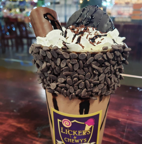 A decadent chocolate milkshake topped with whipped cream, chocolate drizzle, and a cookie, surrounded by chocolate chips.