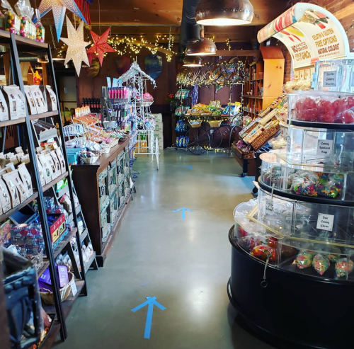 A colorful store aisle filled with various products, candy displays, and decorative items, with blue directional arrows on the floor.