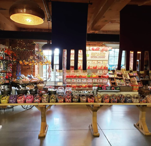 A colorful display of candies and snacks in jars, with shelves of treats in a cozy, well-lit shop.