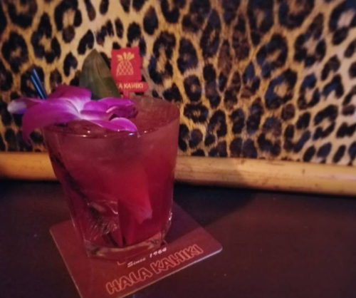 A colorful cocktail garnished with a purple flower, set against a leopard print background.