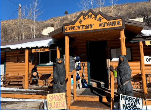 A rustic country store with wooden bear sculptures outside, snow on the ground, and a sign for smoked cheese.