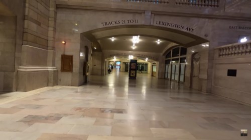 Empty corridor in a grand train station, featuring arched ceilings and signs for tracks and exits.