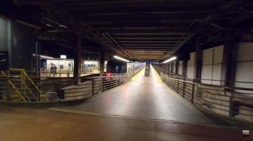 A view of a subway station platform with tracks, waiting area, and a train approaching in the distance.