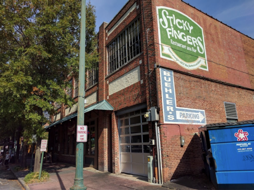 Exterior of Sticky Fingers restaurant with a brick facade, parking signs, and a blue dumpster nearby.