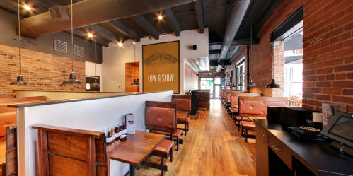 Interior of a restaurant featuring wooden tables, brick walls, and a cozy atmosphere with low lighting.