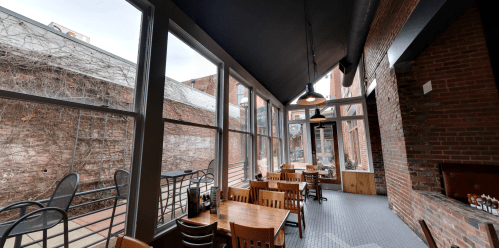 Cozy restaurant interior with wooden tables, large windows, and exposed brick walls, overlooking a courtyard.