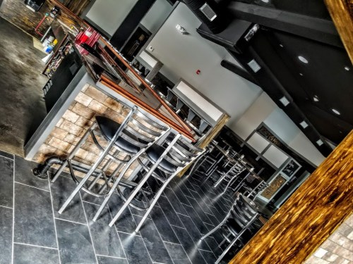 Interior of a modern bar with empty chairs, dark tile flooring, and a sleek wooden counter.