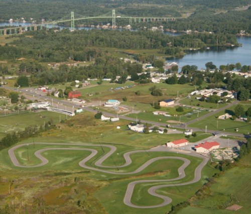 Aerial view of a winding road through green fields, with a bridge and a river in the background.