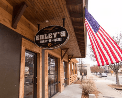 Sign for Edley's Bar-B-Que outside a wooden building, with an American flag hanging nearby.
