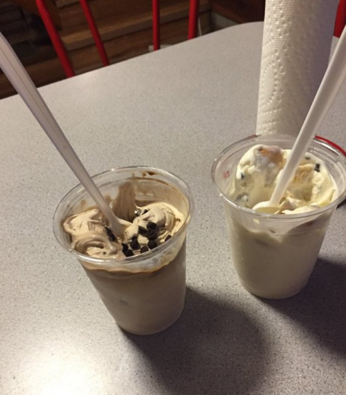 Two cups of ice cream with spoons, one chocolate swirl with chocolate chips and one vanilla with chocolate pieces.