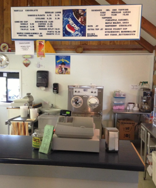 A cozy ice cream shop counter with a cash register, menu board, and ice cream machine.