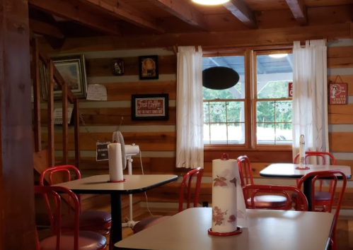 Cozy rustic restaurant interior with wooden walls, red chairs, and tables, featuring a window and decorative items.