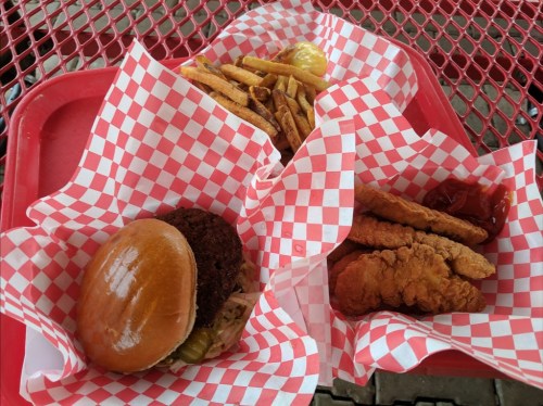 A red tray with two servings: a fried chicken sandwich with pickles and a side of fries, plus crispy chicken tenders and ketchup.