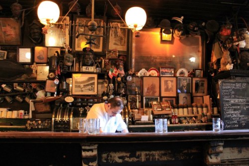 A bartender prepares drinks at a vintage bar adorned with memorabilia and photographs on the walls.
