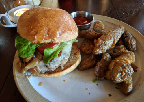 A juicy burger with lettuce, tomato, and cheese, served with seasoned roasted potatoes on a plate.
