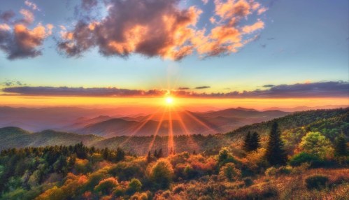 A vibrant sunset over rolling mountains, with colorful clouds and lush trees in the foreground.