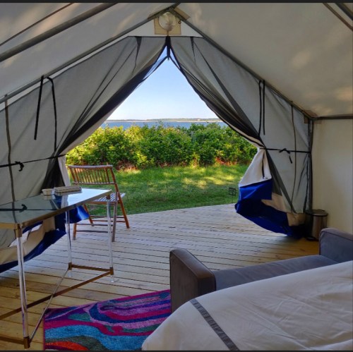View from a tent doorway, showcasing a grassy area and water in the distance, with a chair and table inside.
