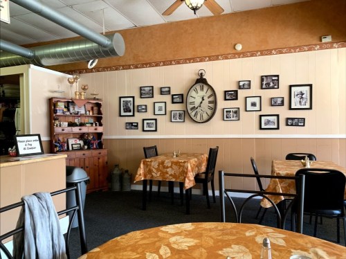 Cozy restaurant interior with orange tablecloths, black chairs, and a wall adorned with framed vintage photos and a large clock.