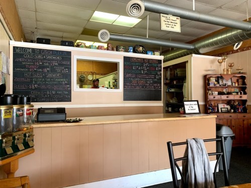 A cozy deli interior with a counter, menu boards, and shelves displaying various items.