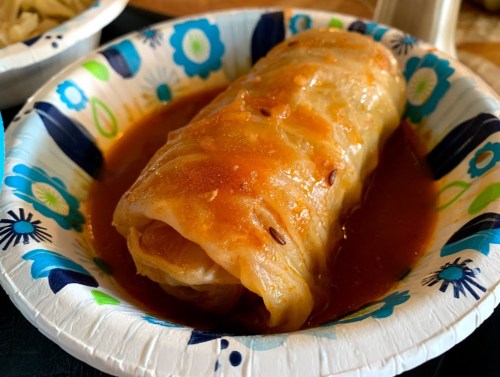 A stuffed cabbage roll in a colorful paper plate, topped with a rich tomato sauce.