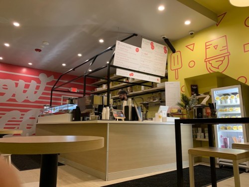 A modern café interior with a counter, menu board, and seating area, featuring bright colors and a welcoming atmosphere.