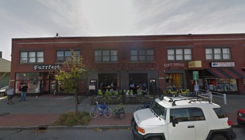 A street view of a brick building with various businesses, including a taco restaurant and a soft serve shop.