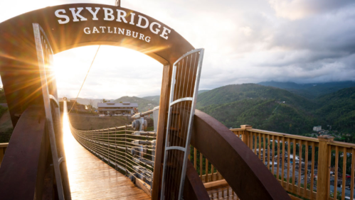A scenic view of the SkyBridge in Gatlinburg, with sunlight shining through the entrance and mountains in the background.