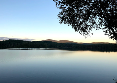 A serene lake at sunset, surrounded by mountains and trees, reflecting the calm sky and water.