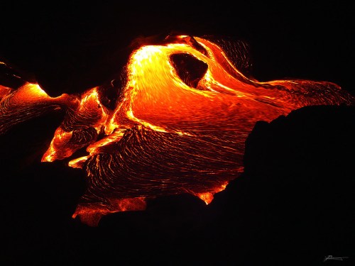 Lava flows glowing brightly between dark rocks, creating a mesmerizing, fluid pattern in a volcanic landscape.