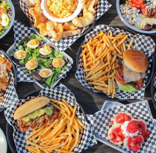A variety of delicious dishes including burgers, fries, salads, and desserts served in checkered paper baskets.
