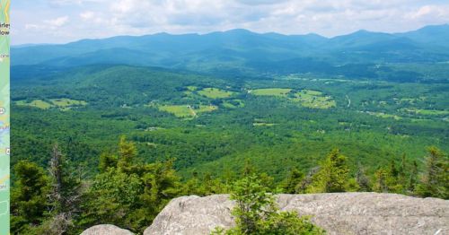 A panoramic view of lush green mountains and valleys under a partly cloudy sky.