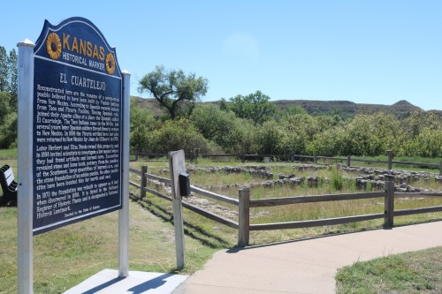 Historical marker for El Cuartelijo in Kansas, with ruins and greenery in the background.
