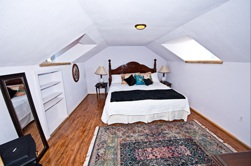 Cozy attic bedroom with a bed, two lamps, and a colorful rug under sloped ceilings and natural light.